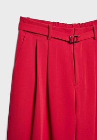 Pantaloni rossi plissettati con cintura in tessuto e fibbia argentata, tessuto liscio e tasche laterali. Vita elasticizzata per maggiore comfort.