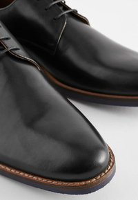 Schwarze Lederdressschuhe mit spitzem Zeh, eleganter Form und Nähdetails entlang der Sohle. Glatte Textur und polierte Oberfläche.