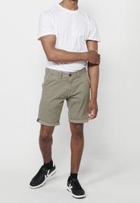 Khaki šortky s ohrnutými lemy, předními kapsami a jedním knoflíkem na zapínání. Spárované s jednoduchým bílým tričkem a černými teniskami.