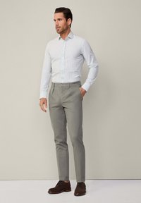 Himmelblau-weiß gestreifes Hemd mit Knöpfen, kombiniert mit grauen Anzughosen und braunen Wildlederschuhen; taillierter Schnitt mit klassischem Kragen.