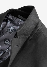 Black blazer featuring a textured collar, floral-patterned gray satin lining, and subtle stitching details along the edges.