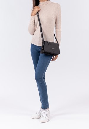 Czarna torba na ramię z fakturowanym wykończeniem, zamkiem błyskawicznym i regulowanym paskiem. Na froncie subtelne logo.