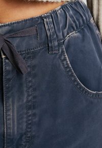 Marinblå byxor med elastisk midja och dragsko, har en framficka och subtil textur. Tyget visar tecken på lätt slitage.