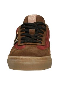 Brown suede sneaker with red accents, black laces, and a patterned side detail. Features a rubber outsole and a logo on the tongue.