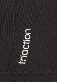 Svart elastisk stoff med ribbet tekstur og hvit "triaction"-logo. Synlig søm gir økt holdbarhet og design.