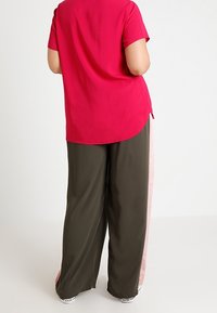 Top a maniche corte magenta abbinato a pantaloni larghi verdi oliva con strisce laterali rosa. Tessuto morbido, vestibilità rilassata, orlo curvo.