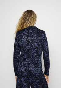 Saklo s leopardím vzorem v námořnické modré a černé barvě, které má slim fit, dlouhé rukávy a špičatý límec. Hladký povrch s jemným leskem.