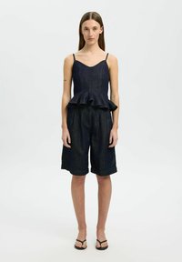 Tmavě modrý peplum top s tenkými ramínky, spárovaný s volně střiženými tmavě modrými šortkami. Hladká textura s jemným leskem.