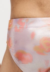Gros plan d'une personne portant des sous-vêtements pastel avec un motif floral doux dans des tons de rose, orange et jaune.