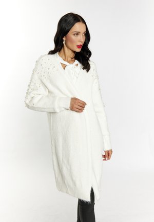 White knitted cardigan with pearl embellishments on the shoulders, wrap design, long sleeves, and side slits for ease of movement.