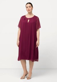 Robe en chiffon bordeaux avec des manches courtes et légères, un décolleté en trou de serrure et un col orné ; la silhouette fluide tombe juste au-dessus du genou.