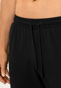 Schwarze Jogginghosen mit einem strukturierten Bund und Zugband, glattem Stoff und einem entspannten Schnitt. Fokus auf Einfachheit und Komfort.