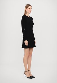 Zwarte geribbelde lange mouw jurk met een uitlopende rok. G gedragen met zwarte puntige hakken met enkelbandjes. Minimalistisch ontwerp en textuur.