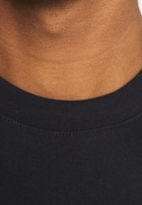 Camiseta de algodón negro de cuello redondo con una textura suave, detalle de costura sutil y un diseño clásico y sin adornos.