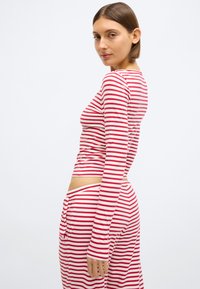 Κόκκινο και άσπρο ριγέ μακρυμάνικο τοπ με εφαρμοστή γραμμή. Μαλακό ύφασμα, στρογγυλή λαιμόκοψη και μακριά μανίκια με κοντό τελείωμα.