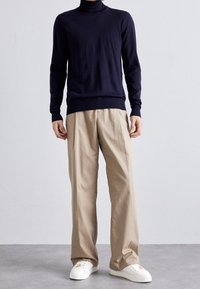 Marinblå turtlenecktröja, figursydd silhuett; i kombination med beiga vida byxor; kompletterad med vita sneakers. Slinky tyg, minimalistisk design.