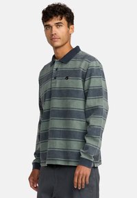 Langärmliges Poloshirt in grünem und marineblauem Streifenmuster, aus Baumwollmaterial, mit einem marineblauen Kragen und kleinem Logodetail auf der Brust.