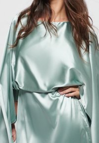 Satiiniwrap-dress mintunvihreänä, jossa on leveä venekaarroke, löysät hihat ja drapoinnilla, luoden sileän ja pehmeän tekstuurin.