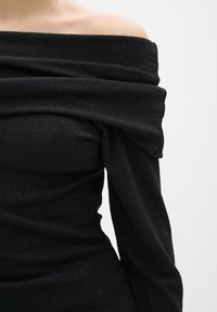 Černý top bez ramínek s drapovaným designem, vyrobený z texturovaného materiálu s jemnými lesky a dlouhými, přiléhavými rukávy.