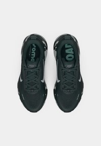 Pár čiernych a šedých bežeckých topánok Nike s podrážkami v camo vzore, viazané, pohľad zhora na bielom pozadí.