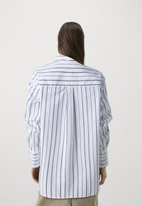 White button-up shirt with blue vertical stripes, featuring a back yoke, long sleeves, and buttoned cuffs, made from lightweight fabric.