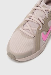 Světlé růžové sportovní boty vyrobené z prodyšného materiálu a semiše. Mají strukturovanou špičku a jasně růžové logo Nike. Zavazování na tkaničky.