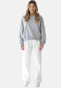 Szara bawełniana bluza z okrągłym dekoltem o luźnym kroju, zestawiona z białymi szerokimi spodniami i białymi trampkami, na jednolitym tle.