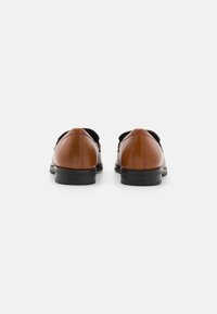 Zapatos de cuero marrón con un acabado suave, puntas redondeadas y suelas de goma negras. Diseño minimalista, con detalles de costura en contraste.