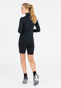 Zwart atletisch langemouwen top en shorts met een aansluitend ontwerp. De top heeft een hoge kraag en logodetail op de achterkant.