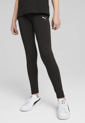 Leggings noirs en tissu extensible avec un design ajusté. Présente un petit logo blanc de Puma sur la cuisse. Le modèle porte des baskets blanches.