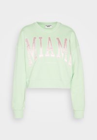 Felpa cropped verde menta realizzata in tessuto morbido, con "MIAMI" in lettere rosa lucide sulla parte anteriore. Presenta polsini a coste.