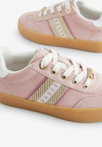Adidași roz din suede, cu o dârnă bej împletită și textul 'BAKER', șireturi albe și talpă din cauciuc de culoare maro. Ochiurile din argint completează designul.