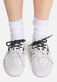 White suede athletic shoes with black accents and black and white striped laces, worn with ribbed white crew socks.