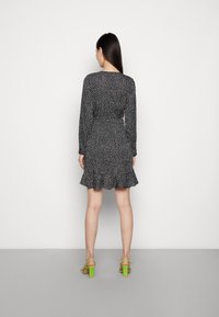 Svartrandig klänning i svart med vita prickar, långa ärmar och utsvängd nederkant. Bärs med gröna klacksandaler, mot en enkel bakgrund.