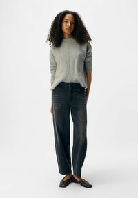 Maglione grigio a maglia con scollo rotondo, abbinato ajeans in denim scuro a vestibilità ampia e scarpe basse marroni. Design semplice e testurizzato.