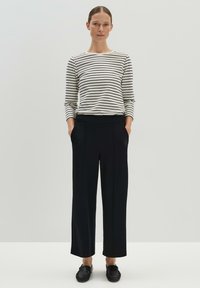 Pantalons larges noirs avec poches associés à un haut à manches longues rayé noir et blanc. Le matériau semble doux ; design à taille cintrée.