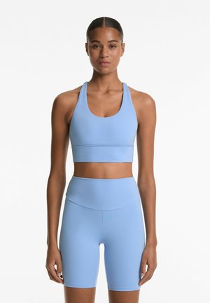 Blue sports bra with a scoop neckline and wide straps, paired with high-waisted blue shorts. Both feature a smooth, stretchy fabric.