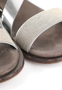 Gros plan sur des sandales grises avec des brides en tissu texturé et des semelles intérieures douces et rembourrées présentant une légère usure sur les bords.