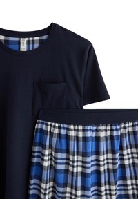 T-shirt en coton bleu marine avec une poche, associé à une jupe à carreaux bleu comprenant des nuances de bleu et de blanc, froncée à la taille.