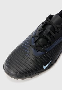 Crne sintetičke cipele s teksturiranim gornjim dijelom, brazdama i plavim Nike logotipom. Imaju crne vezice i izdržljiv gumeni potplat. Kompaktan dizajn.