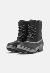 Las botas negras de tobillo impermeables cuentan con una suela de goma texturizada, acentos grises y un diseño de cordones. La parte superior está hecha de un suave material de ante.