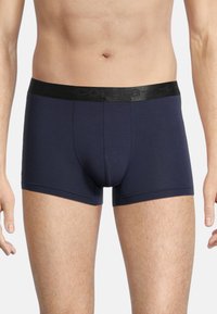 Navy blue boxer briefs made from stretchy fabric. Features a black elastic waistband with logo. Smooth texture, fitted design, and mid-thigh length.