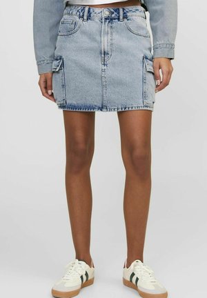 Minifalda de denim en azul claro, con bolsillos frontales, dos bolsillos laterales de estilo cargo y un corte recto. Combinada con zapatillas blancas.