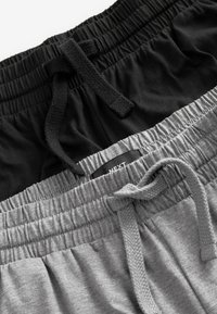Pantaloni de trening negri și gri cu talie elastică, având un material texturat și șnururi de ajustare la talie. Eticheta brandului este vizibilă pe pantalonii gri.