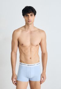 Helle blaue Boxershorts mit einem weißen Bündchen, das das schwarze "GANT"-Logo zeigt. Glatte Textur, eng anliegendes Design und mittellange Passform bis zum Oberschenkel.