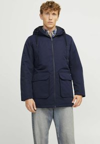 Mornarsko modra, parka srednje dolžine s kapuco, dvema velikima sprednjima žepe in zadrgo. Material se zdi gladek z mat končnim obdelavo.
