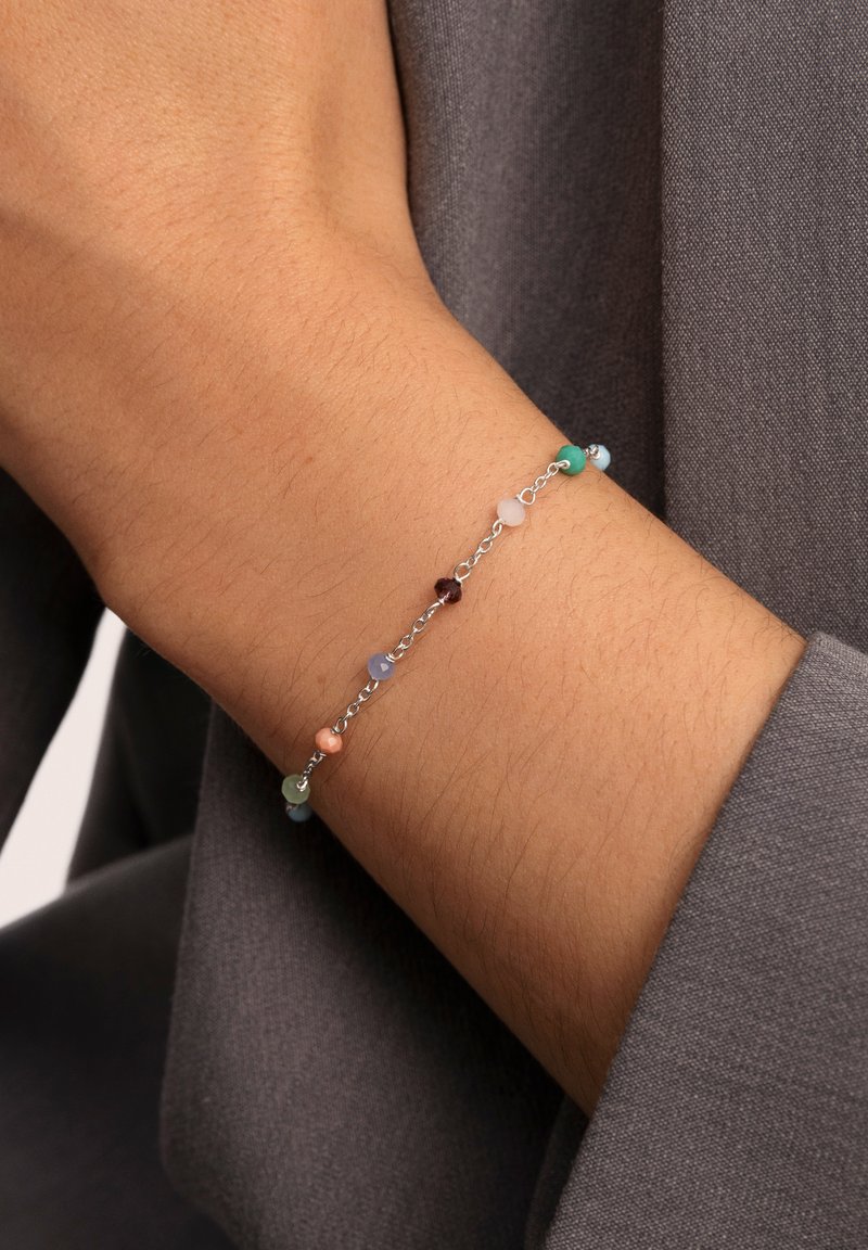 Silver chain bracelet with multiple small round beads in colors including blue, green, peach, and brown. Worn on a wrist.