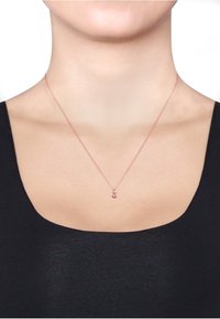 Halskette aus Roségold mit einer zarten Kette und kleinen runden Anhänger, präsentiert vor einem schwarzen Oberteil und neutralem Hintergrund.