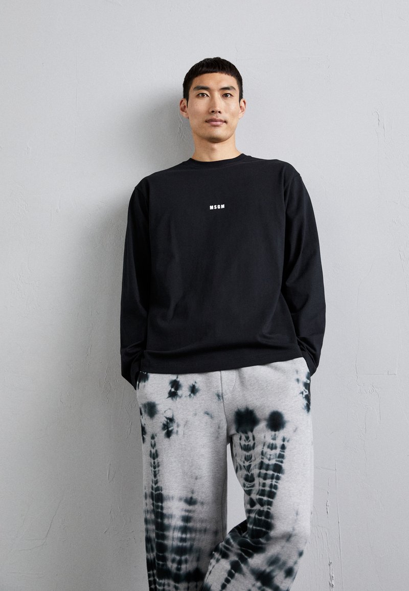 Black long-sleeve sweatshirt with white logo on the chest, paired with gray tie-dye sweatpants featuring dark green patterns.