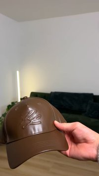 Ruskea lippalakki, jossa on kiiltävä viimeistely ja kohokuvioitu logo etupaneelissa. Lippalakissa on kuusi ommeltua ilmanreikää ja kaartuva lippa.